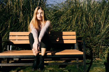 açık havada güneşte bir bankta oturmuş, poz güzel kendine güvenen genç kız modeli
