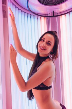 gülümseyen bir dikey bronzlaşma yatak ultraviyole ışınları altında güneşlenme mutlu genç kız