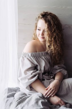 içinde bir güzel kıvırcık genç kadın oturur pencerenin bir perde ile gülümseyen