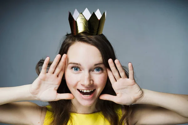 Feliz chica de ojos azules en un vestido amarillo se ríe, en su cabeza una corona de oro — Foto de Stock