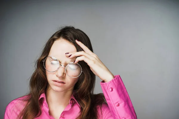 Cansada joven trabajadora de oficina con una camisa rosa y gafas cerró los ojos, dolor de cabeza — Foto de Stock