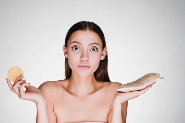 Uma menina bonita cuida de seu rosto e corpo, segura uma esponja e um loofah em suas mãos — Fotografia de Stock