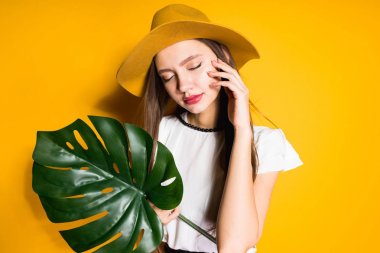 emin uzun saçlı kız modeli şık şapka içinde tutan sarı bir arka plan üzerinde poz bir yaprak yeşil gözler kapalı