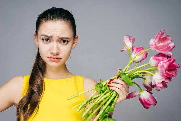 Грустная сердитая девушка в желтом платье держит букет розовых цветов — стоковое фото