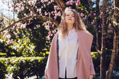 çekici kıvırcık kadın parkta bir sıcak bahar gününde yürüyüş, poz ve gülümseyen pembe bir ceket