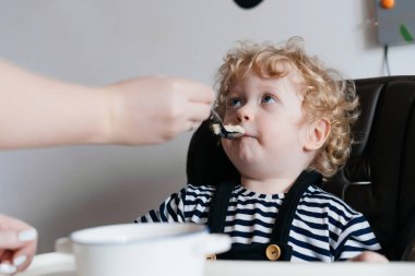 şefkatli anne küçük kıvırcık çocuğunu oğlunun yararlı püresi ile bir kaşık ile beslenir