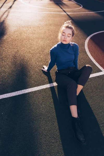 Vertrouwen stijlvolle jong meisje model in een blauwe trui poseren op een sportveld in de stralen van de ochtendzon — Stockfoto