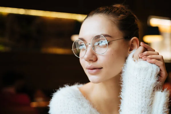 放課後カフェで座っているし、窓の外に見える白いジャケットとメガネの素敵なかわいい女の子学生 — ストック写真