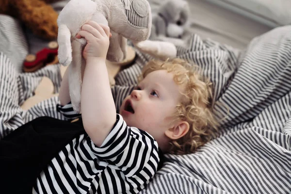 Kudrnatá malý chlapeček leží na posteli a hraje si s jeho oblíbená Plyšová hračka — Stock fotografie