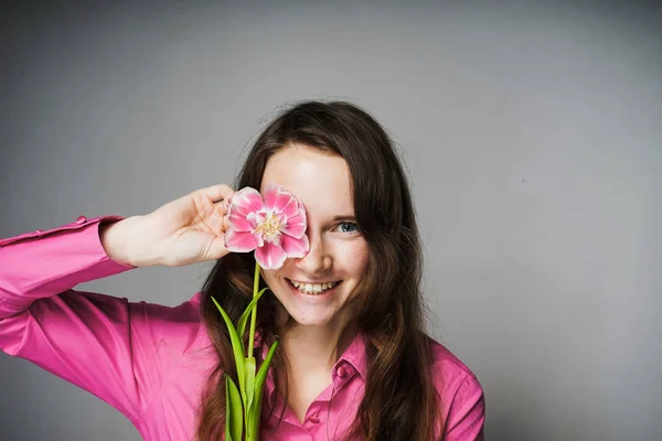 Jovem mulher feliz em uma camisa rosa sorri, mantém uma flor rosa perfumada no rosto — Fotografia de Stock