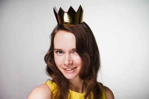 Bela jovem mulher em um vestido amarelo olha para a câmera e sorri, na cabeça uma coroa de ouro — Fotografia de Stock