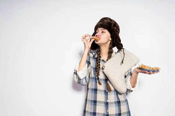 Faim fille russe dans un chapeau de fourrure tient des bottes en feutre chaud et mange des crêpes chaudes, célèbre Shrovetide — Photo