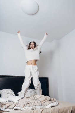 mutlu genç kız yatakta atlama ve gülerek beyaz pijama