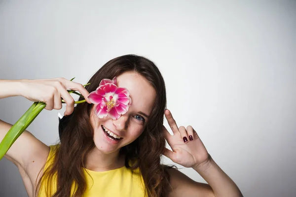 Szczęśliwy uśmiechający się dziewczyna w żółta sukienka posiada różowy pachnący kwiat na twarz — Zdjęcie stockowe