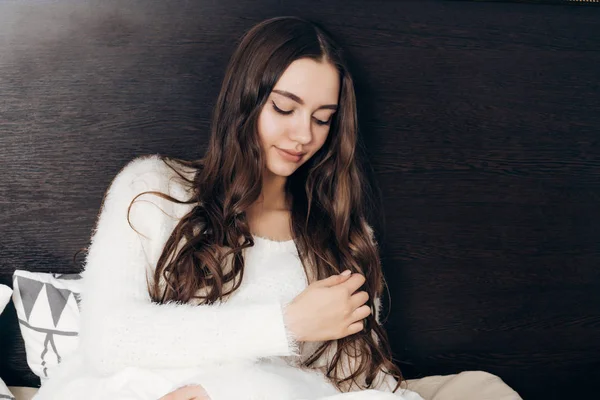 Beautiful long-haired girl sits in bed, resting after a hard day's work — Stock Photo, Image