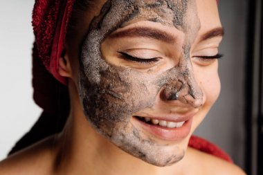 güzel genç kız başında bir havlu ile uygulanan bir yararlı kil maskesi yüzünde, gülümseyen