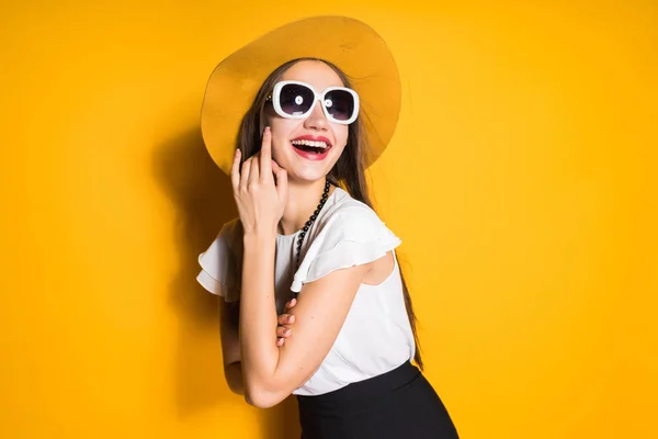 Feliz chica sonriente en sombrero de moda y gafas de sol posando sobre fondo naranja — Foto de Stock