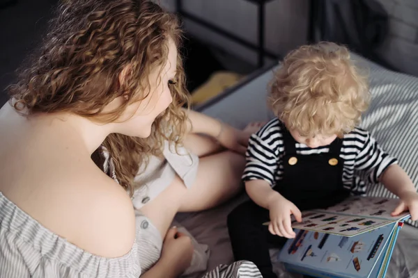 Přátelská rodina, mladá matka se dívá na své malé dítě, chlapec se učí číst — Stock fotografie