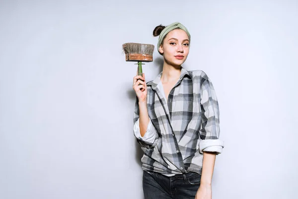 Красивая молодая девушка в клетчатой рубашке держа кисть для покраски стен, ремонт в квартире — стоковое фото