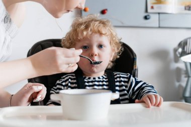 Aile yemeği, bakmakta genç bir anne mutfakta yararlı yulaf lapası ile küçük kıvırcık oğlu beslemeleri
