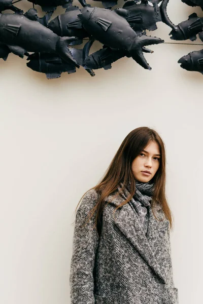Chica de la ciudad con estilo de pelo oscuro en abrigo gris de moda posando contra la pared blanca al aire libre — Foto de Stock