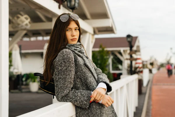 Fille aux cheveux foncés en manteau gris élégant marchant à l'extérieur, posant et regardant la caméra — Photo