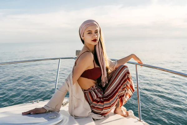 a stylish rich woman with a headscarf sitting on her white yacht in the llah of the sun, sailing to the islands