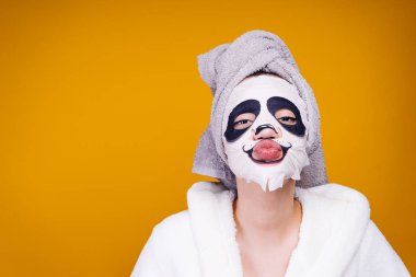 garip bir genç kız başını ve beyaz banyo bornoz havlu ile yüz maskesi panda yüzü olan bir hava öpücük gönderir