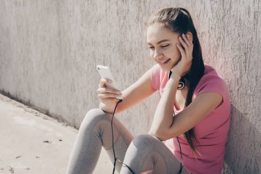 güzel genç kız güç ve enerji eğitim, açık havada oturma, onun smartphone bakıyor ve gülümsüyor önce kazanıyor