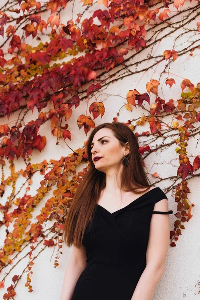 luxurious rich woman in a black dress, with long hair, posing in her garden against the wall, enjoying the rest
