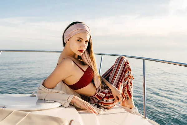 Una chica elegante de lujo en ropa de verano descansa en su yate blanco, disfruta de la vista del mar y el sol —  Fotos de Stock