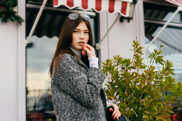 Élégante fille aux cheveux bruns en manteau gris posant sur les rues de la ville — Photo