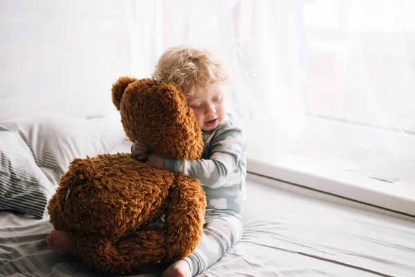 Милий маленький кучерявий хлопчик обіймає свою улюблену фаршировану іграшку — стокове фото