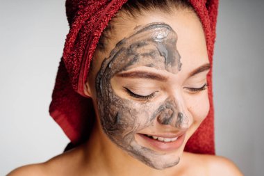 güzel genç kız başında bir havlu ile uygulanan bir yararlı kil maskesi yarım yüz, gülen