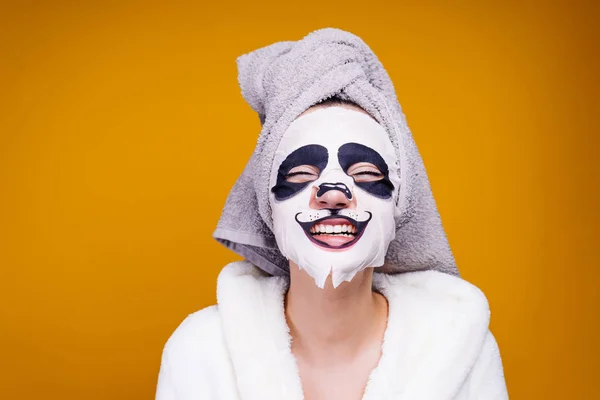 Śmieszne, młoda dziewczyna z ręcznikiem na głowie i uśmiechy biały szlafrok, na jej twarz w maskę z twarzy panda — Zdjęcie stockowe
