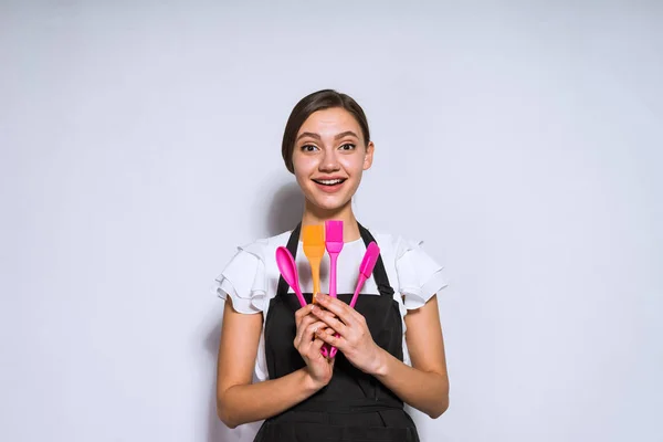 Schöne junge Köchin in schwarzer Schürze mit Werkzeugen zum Kochen und Backen — Stockfoto