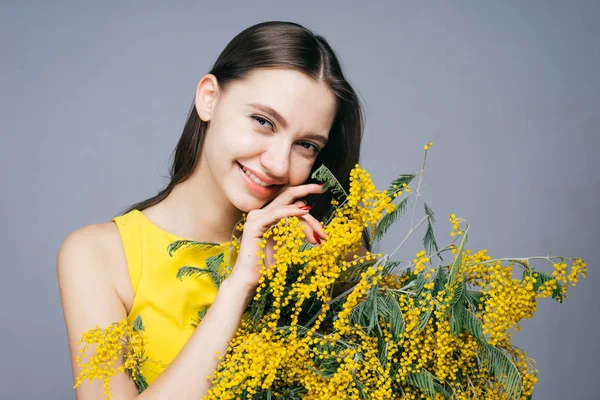 Feliz joven en vestido amarillo sostiene un gran ramo de una mimosa amarilla fragante, sonriendo — Foto de Stock