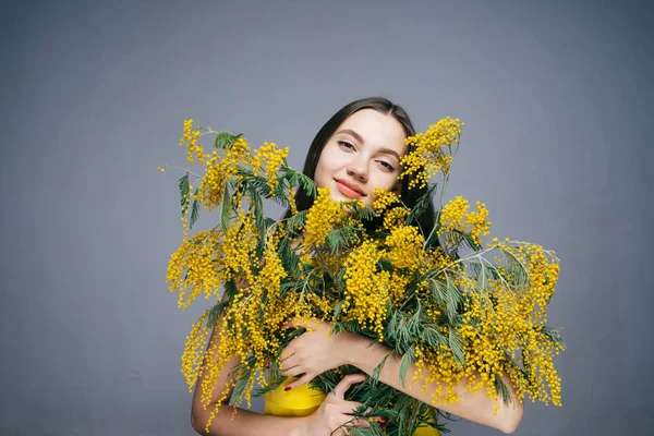 Menina feliz em um vestido amarelo detém um grande buquê de uma mimosa amarela perfumada, goza de primavera e calor — Fotografia de Stock