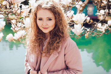 pembe bir ceket bir çiçek kokulu Manolya ve sıcaklık göl yanındaki parkta zevk kıvırcık genç kadın