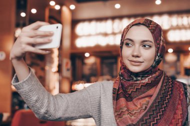 bir başörtüsü rahat bir oryantal kafede oturan ve bir selfie yapma güzel Arap kızla
