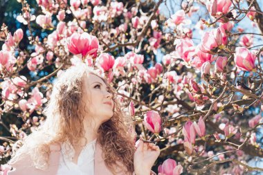 kıvırcık genç kadın güneş altında bir parkta bir kokulu pembe Manolya sahiptir