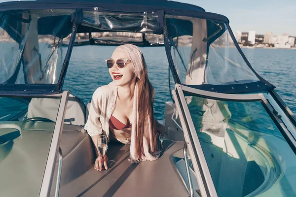 Una mujer joven de lujo en gafas de sol ríe, disfruta de vacaciones y viaje por el mar en un yate —  Fotos de Stock