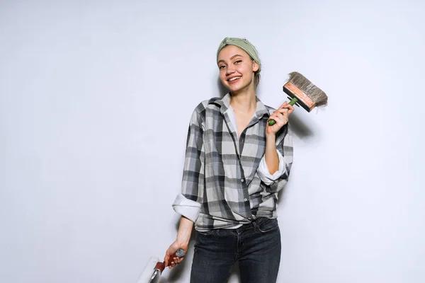 Счастливая юная художница держит кисть и ролик для покраски стен, улыбаясь — стоковое фото