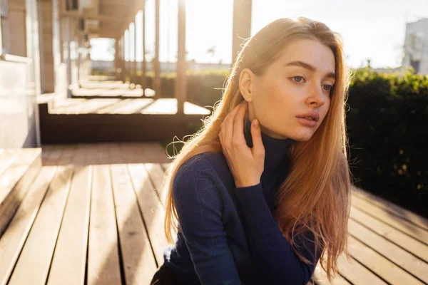 Krásná blond modelka dívka v modrém svetru sedí venku na slunci, které představují — Stock fotografie