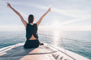 siyah yaz elbiseli bir genç kız beyaz bir yatta oturur, uzun zamandır beklenen bırak sahiptir ve şampanya içer