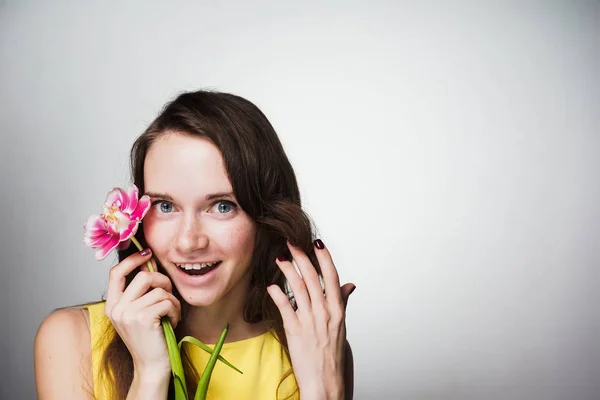 Sorridente ragazza dagli occhi azzurri in un abito giallo tiene un fiore rosa fragrante, sembra felice — Foto Stock