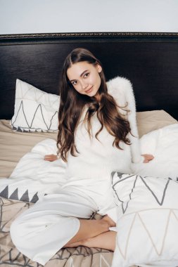 güzel uzun saçlı kız yatakta bir iş günü sonra dinlenme beyaz pijama yalanlar içinde gülümseyen