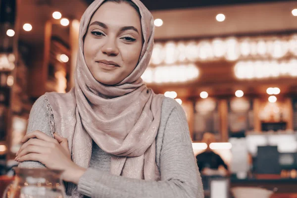 Beautiful Arab girl with headscarf sitting in a cafe at a table and smiling, waiting for her food — Stock Photo, Image