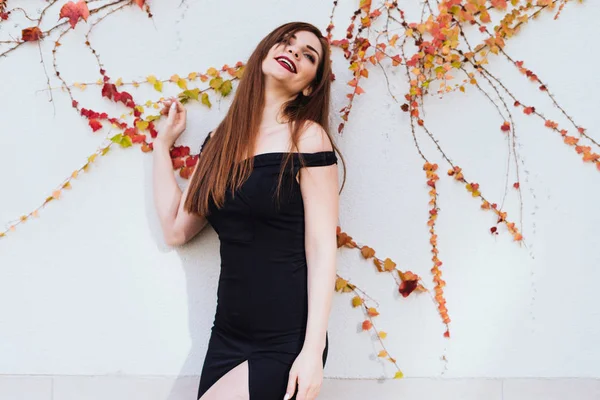Hermosa chica de pelo largo en un vestido negro elegante posando contra la pared, riendo y descansando — Foto de Stock