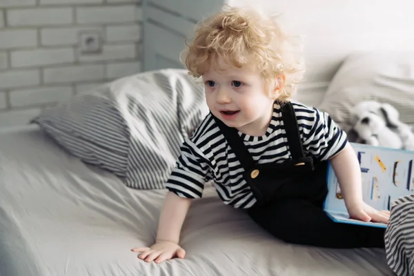 Roztomilé kudrnaté miminko chlapeček v obleku se sedí na posteli a s úsměvem — Stock fotografie